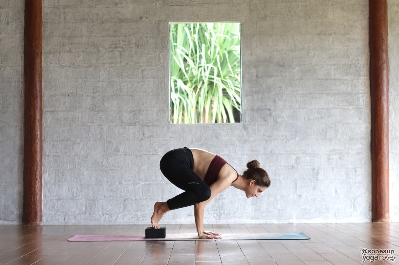 beginner student practicing crow pose with yoga block under feet.