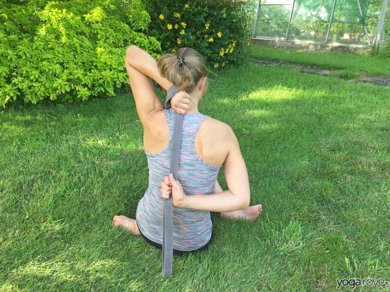 yoga students practicing cow face pose with strap for pain between shoulder blades.