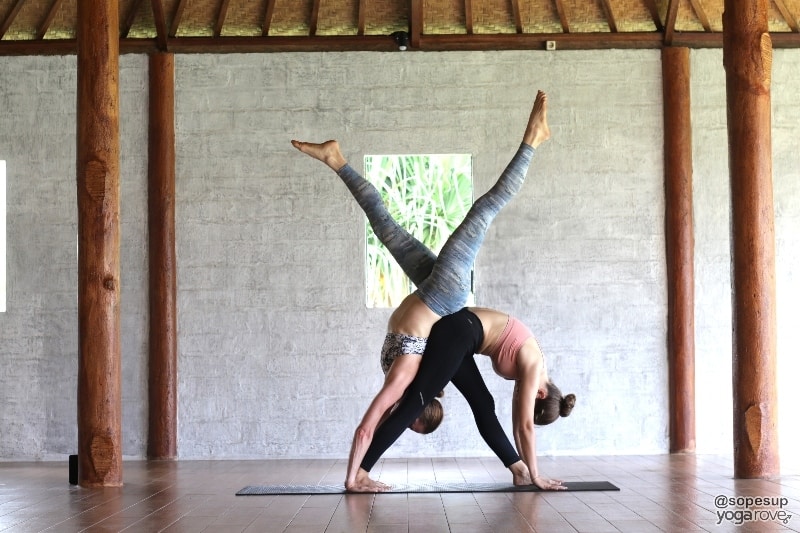 yoga students practicing partner yoga- pyramid pose and handstand