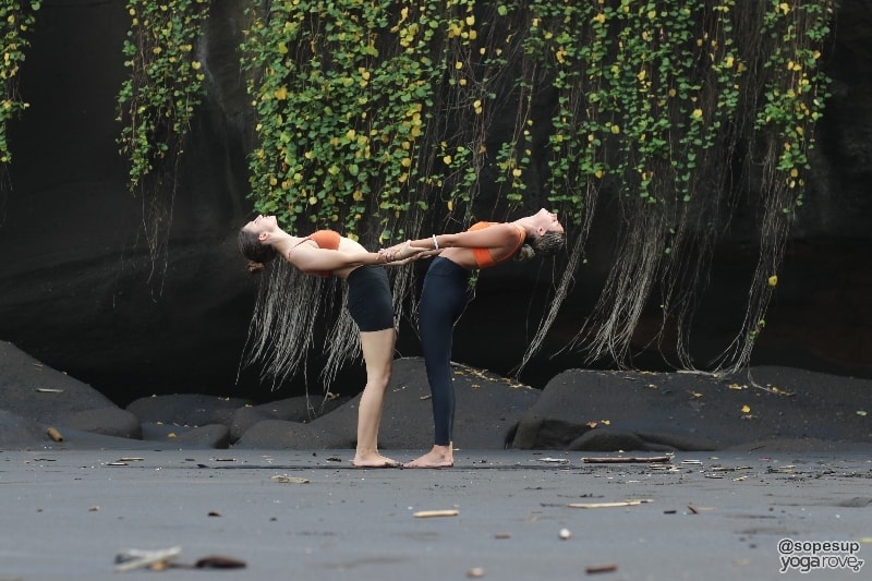 two yogis practicing standing backbend pose in partner yoga.