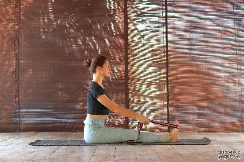 yoga student practicing seated forward fold with yoga strap.