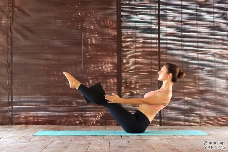 yogi practicing boat pose with block between thighs.