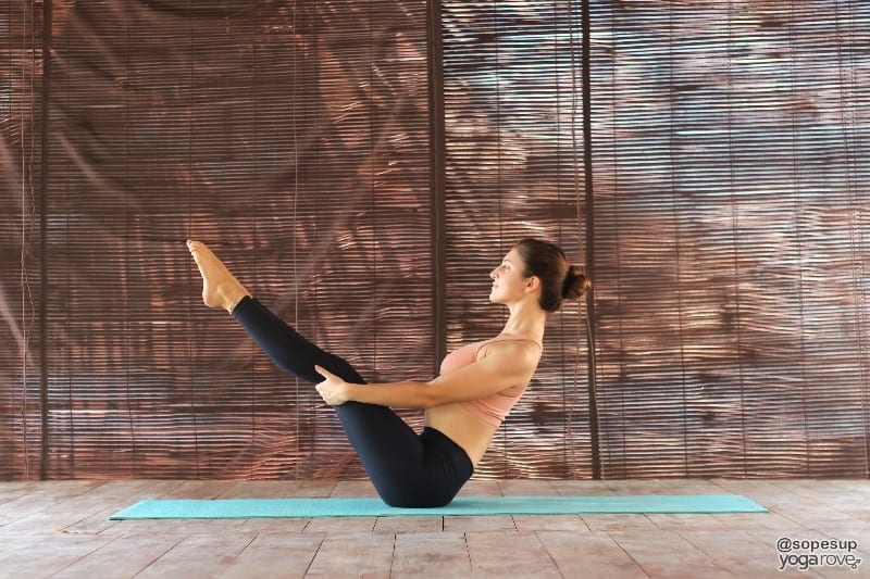 yogi practicing boat pose holding legs.