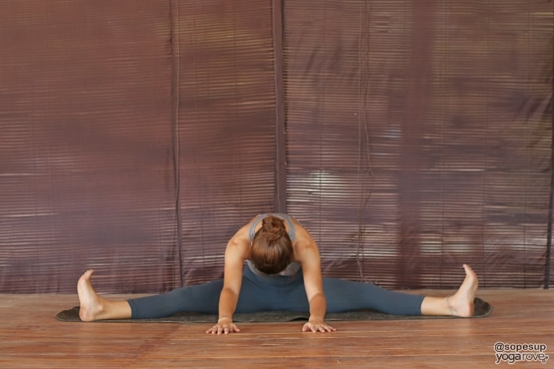 yogi practicing wide legged seated fold on floor.